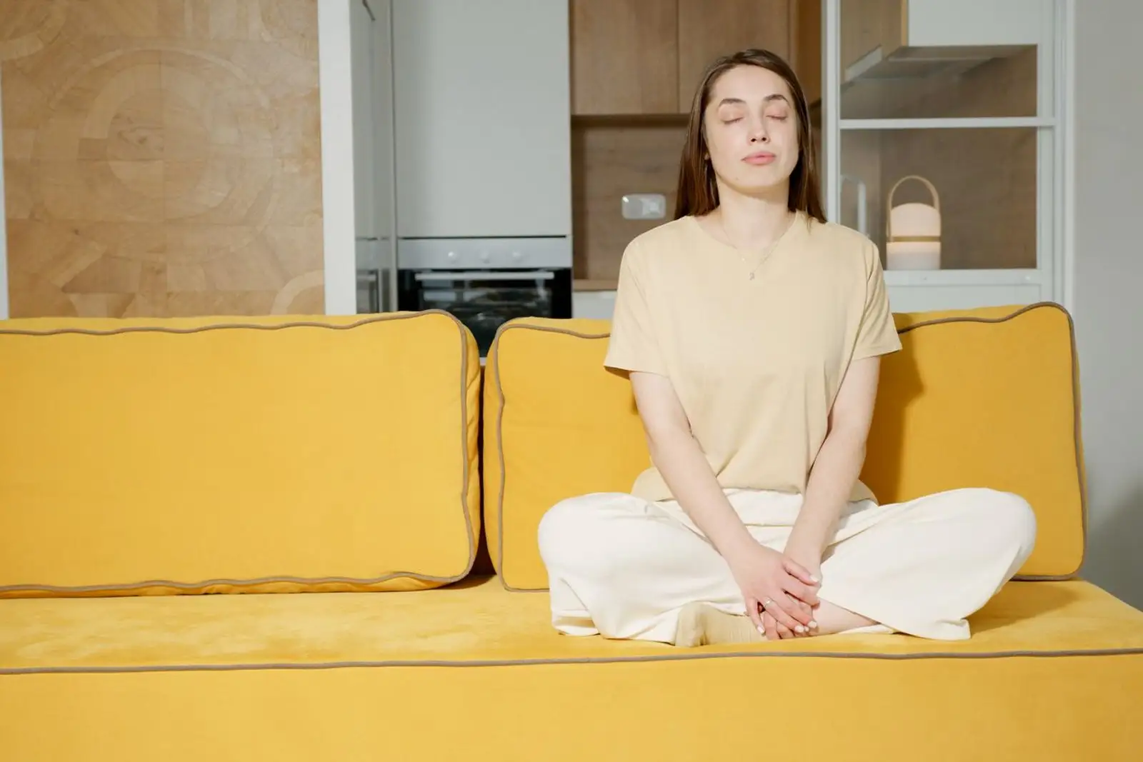 Une personne assise dans un fauteuil confortable, yeux fermés, respirant calmement dans un salon lumineux